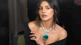 Priyanka Chopra wearing a black off-shoulder gown and a striking emerald and diamond necklace with a matching emerald ring, photographed at a luxury event.