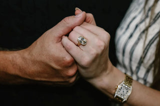 Close-up of Taylor Swift’s hand wearing an old mine cushion cut diamond engagement ring on a yellow gold band, while holding Travis Kelce’s hand.