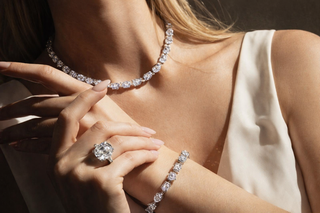Luxury diamond necklace with matching tennis bracelet and large cushion cut engagement ring on model in warm sunlight