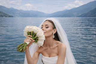 Bride by a lakeside holding a bouquet of white roses wearing pear shaped diamond drop earrings and a strapless wedding gown