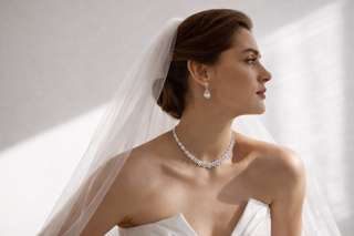 Bride wearing a diamond necklace and drop earrings with a soft white veil and strapless wedding gown in natural light