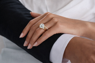 Close-up of a diamond engagement ring with a round center stone and diamond band worn on hand in a refined, minimal setting