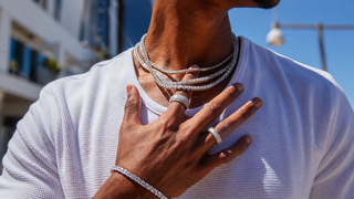 Luxury men’s diamond jewelry with layered tennis necklaces, statement rings, and a diamond bracelet styled with a white textured shirt