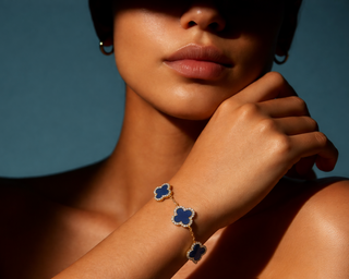 Close-up editorial shot of a woman wearing a gold bracelet with blue clover motifs and diamond detailing under warm dramatic lighting