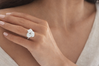 Three stone diamond ring with oval and pear shaped diamonds on a woman's hand against a soft neutral background