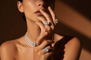 Luxury close-up portrait of a woman wearing multiple diamond statement rings and layered diamond necklaces under warm editorial lighting.