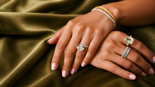 Elegant hands with multiple diamond rings and stacked bracelets resting on olive green satin fabric