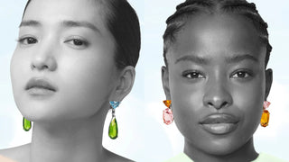 Prada campaign featuring two models in monochrome with bold gemstone earrings — one wears green and blue drop earrings, the other wears pink and orange.