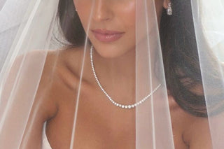 Bride wearing a diamond tennis necklace and drop earrings under a sheer bridal veil in soft natural light