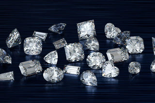 A variety of loose diamonds in different shapes and cuts including cushion, emerald, pear, round, heart, and princess, placed on a dark blue textured background