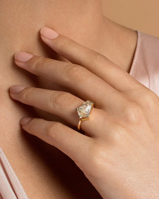 Close up of a geometric shield cut diamond solitaire ring set in yellow gold, worn against soft blush satin for an elegant contemporary look.