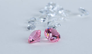Two vivid pink lab-grown diamonds placed in front of scattered white diamonds, highlighting the contrast between colored and classic stones.