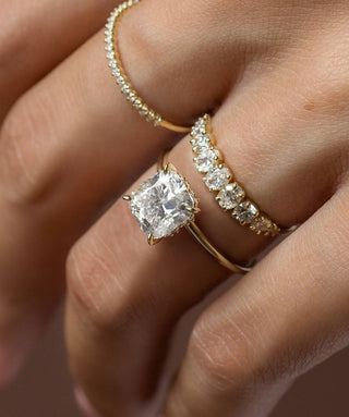 Close up of a cushion cut diamond solitaire ring paired with sparkling diamond eternity bands in yellow gold, highlighting the beauty of layered bridal jewellery.