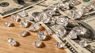 Loose brilliant cut and fancy cut diamonds scattered across overlapping US $100 bills on a warm wooden surface, creating a luxurious composition centred on diamonds, money and investment.