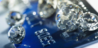 Close-up of loose cut diamonds placed on top of a blue credit card, symbolizing the financial perception of diamonds as investments.