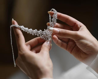 Close-up of a bride holding a delicate diamond bridal necklace with soft floral detailing against a blurred wedding gown background