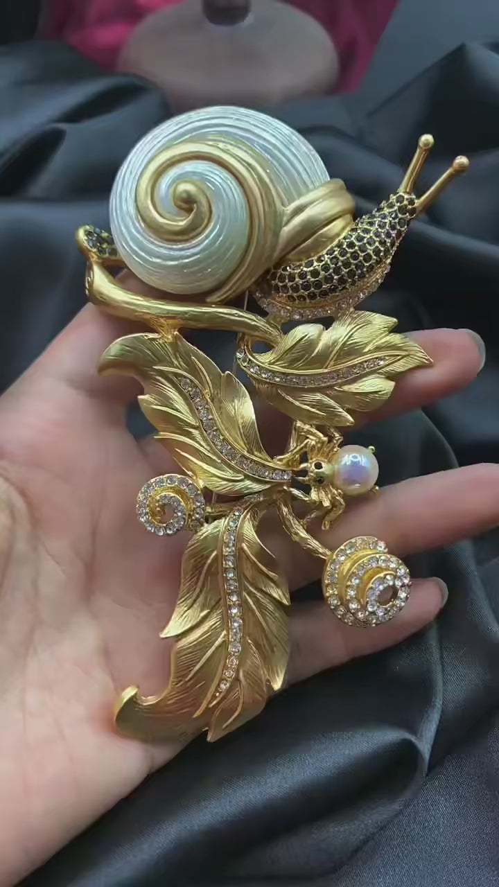 An elegant snail brooch in gold and white, embellished with leaves, perfect for adding a touch of nature to any outfit.